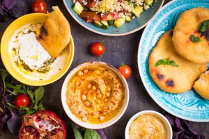 Table served with middle eastern traditional vegetarian dishes. Hummus, tahini, pitta, couscous salad and buttermilk dip with olive oil. Dinner party